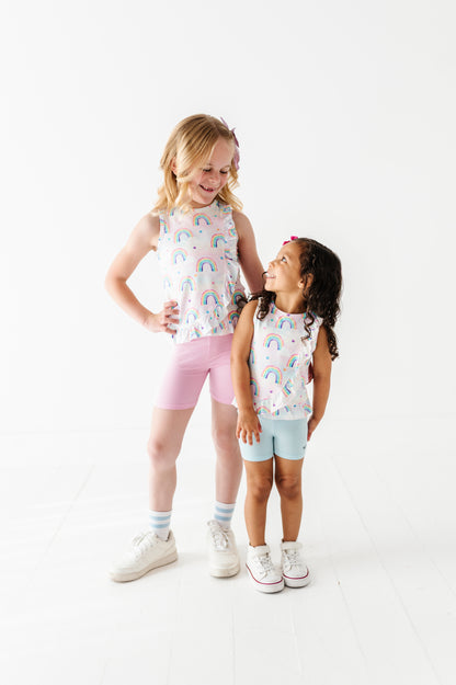 Two young girls wearing matching bamboo outfits with rainbow patterns on a white background