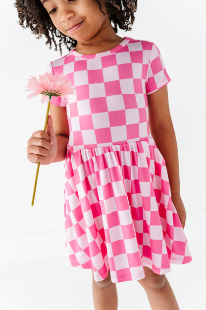 Child wearing a pink and white checkered dress holding a flower.
