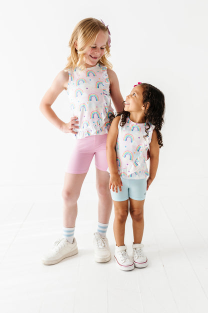 Two young girls wearing matching bamboo cotton outfits with watercolor rainbow patterns on a white background