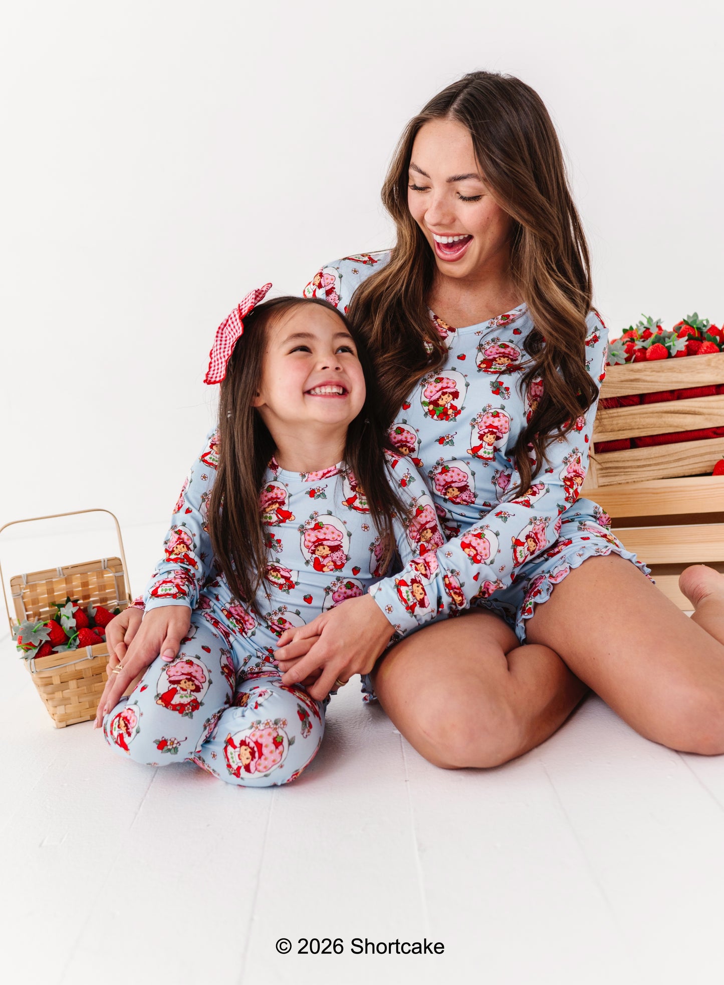 Mother and daughter wearing matching Strawberry Shortcake™ bamboo pajamas sitting on a white background.
