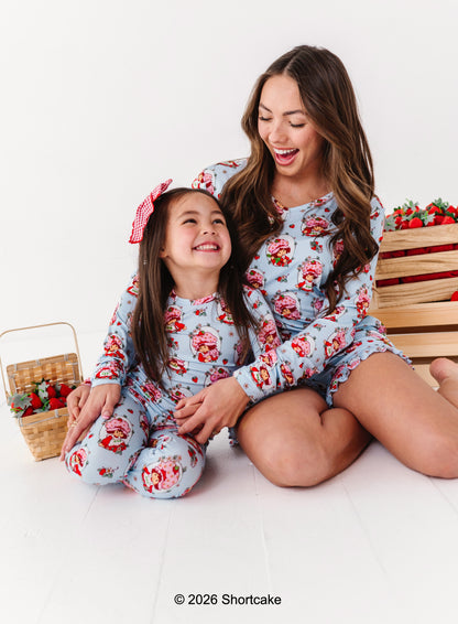 Mother and daughter wearing matching Strawberry Shortcake™ bamboo pajamas sitting on a white background.