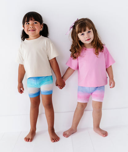 Two children holding hands wearing coordinating ombre biker shorts on a white background