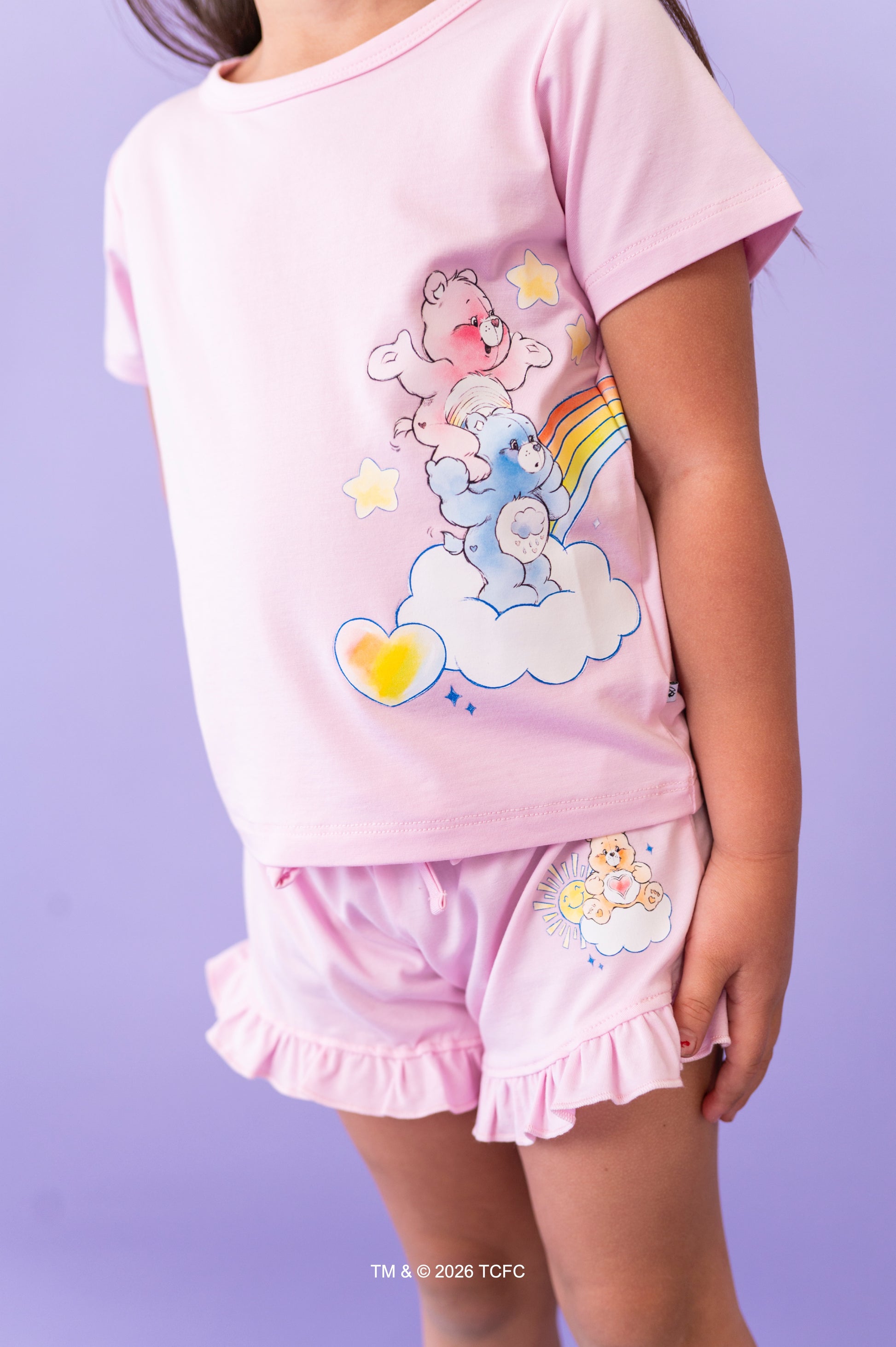 Child wearing a lilac short set with cartoon Care Bears™ design on a purple background