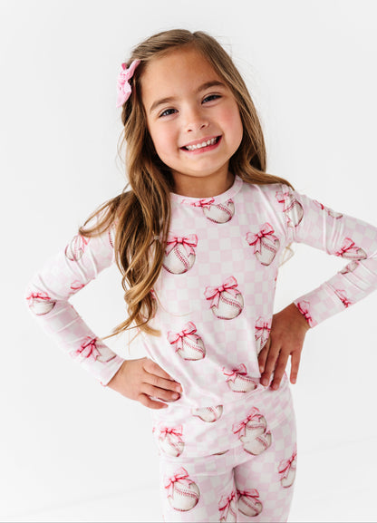 Young girl wearing a bamboo pj set with pink bow and baseball  patterns on a white background