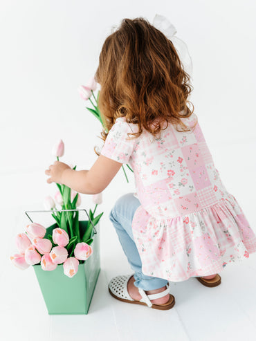 Child in a floral bamboo-cotton shirt holding pink tulips next to a green vase on a white background