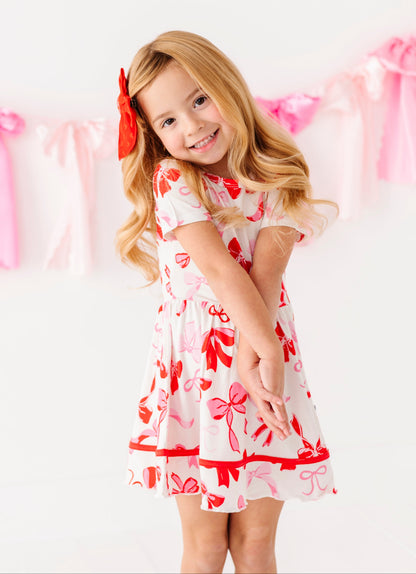 Toddler girl wearing bamboo twirl dress with red and pink bow details