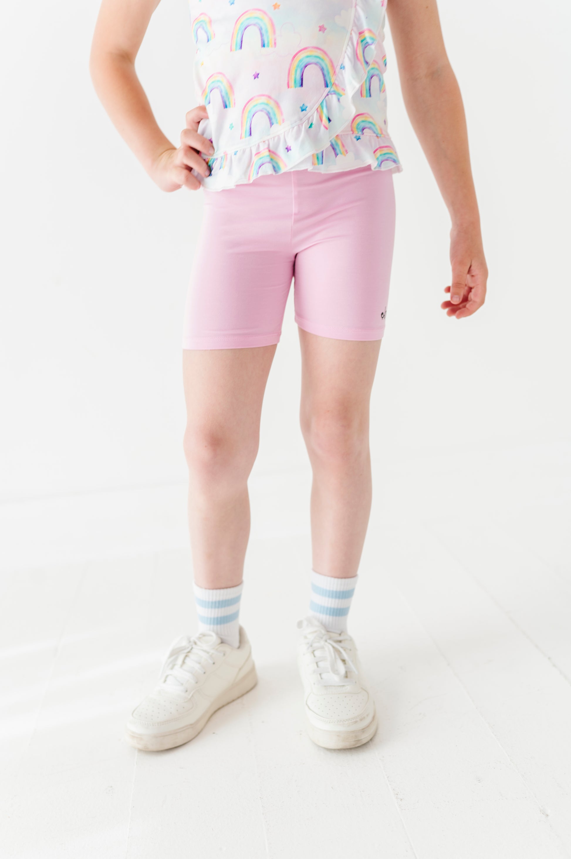 Child wearing a rainbow-patterned bamboo cotton peplum top and pink bamboo biker shorts on a white background