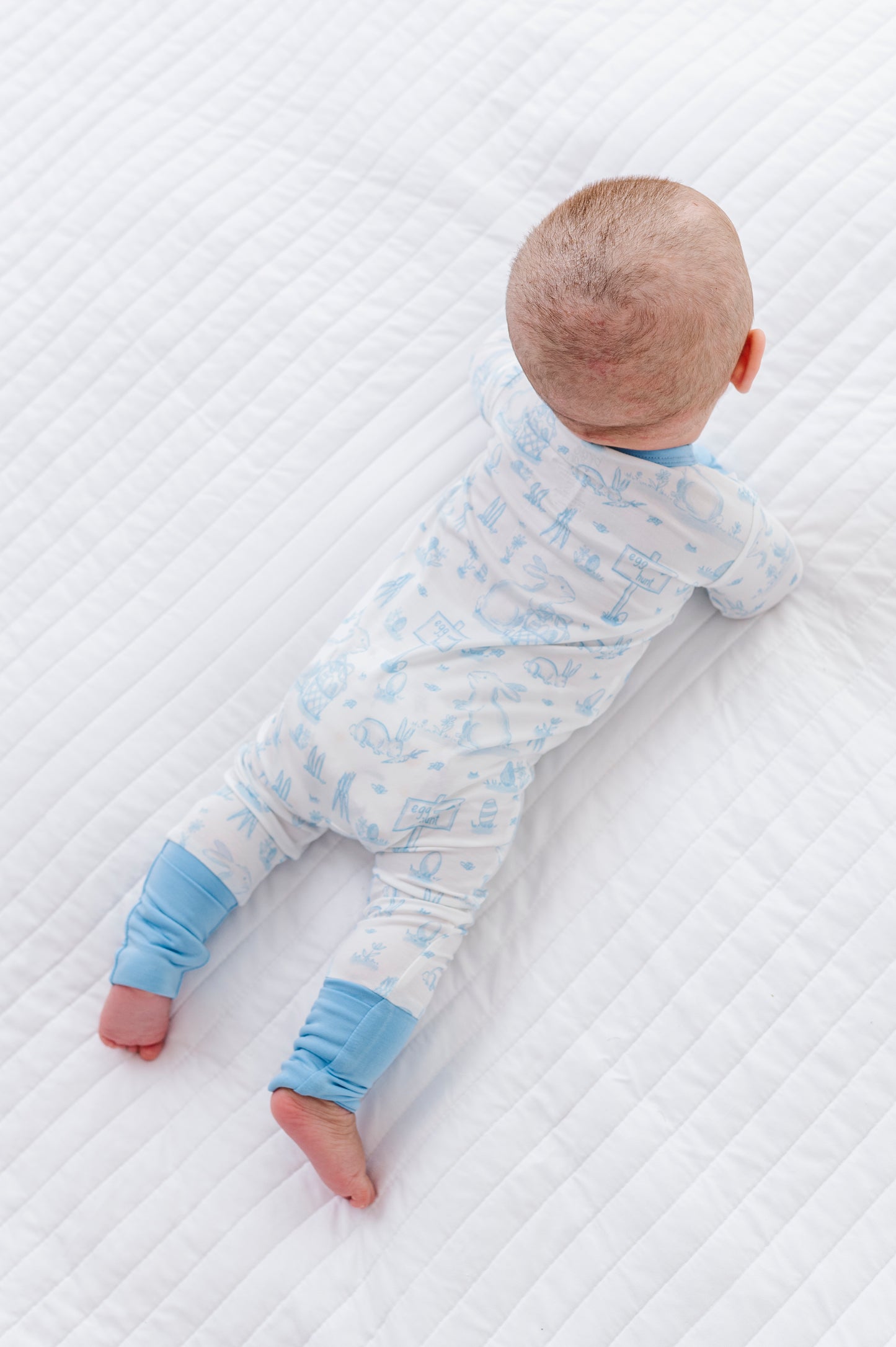 Baby lying on a textured white surface wearing a blue and white bamboo Easter onesie.
