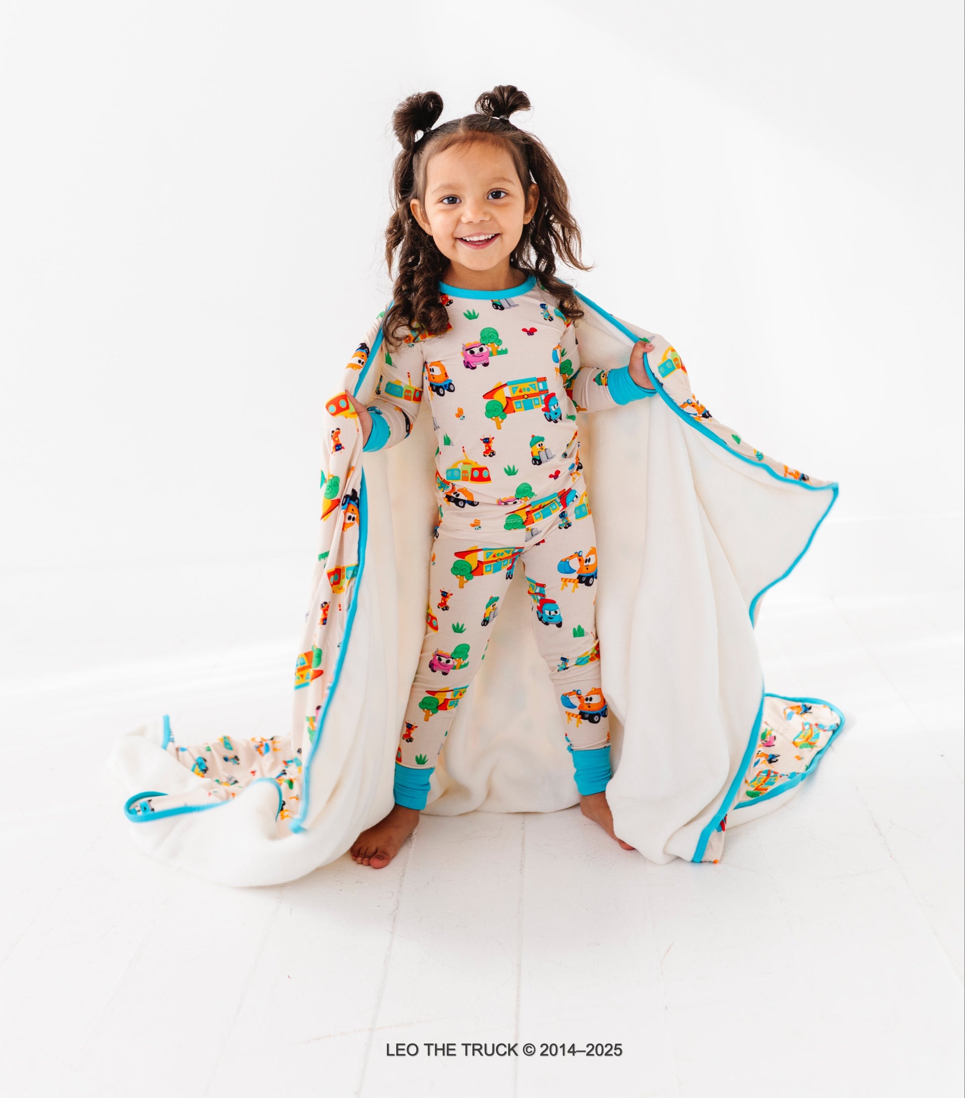 Little girl wearing colorful Leo the Truck bamboo pajamas on a white background