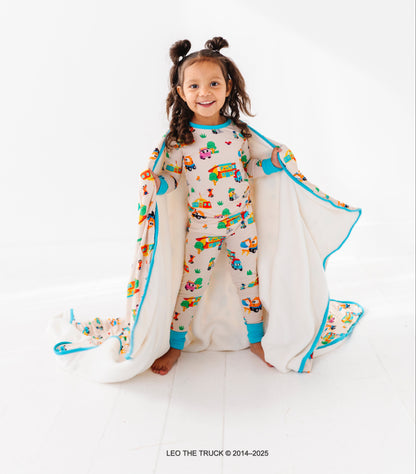 Little girl wearing colorful Leo the Truck bamboo pajamas on a white background