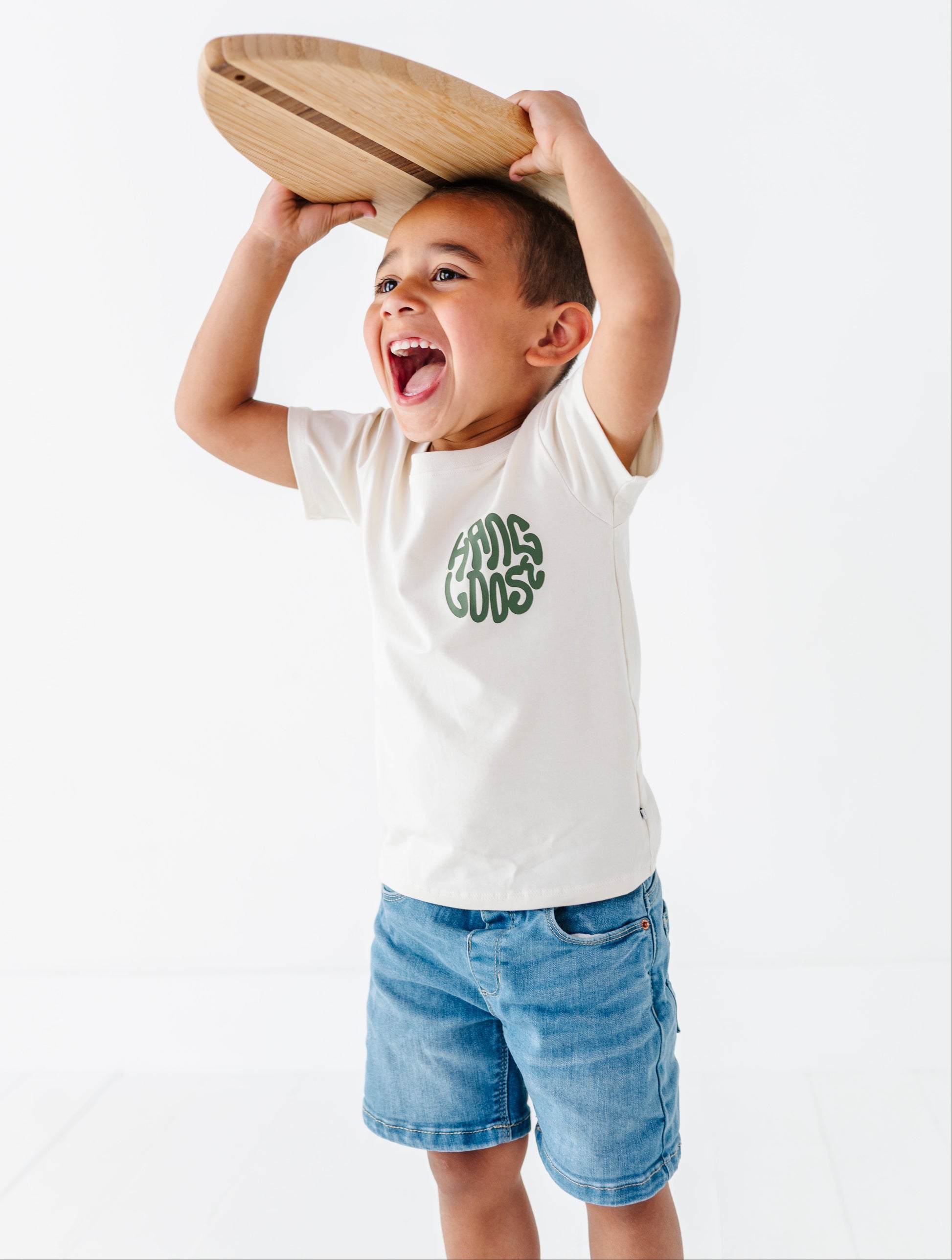 Child holding a wooden surfboard  above their head with a white background