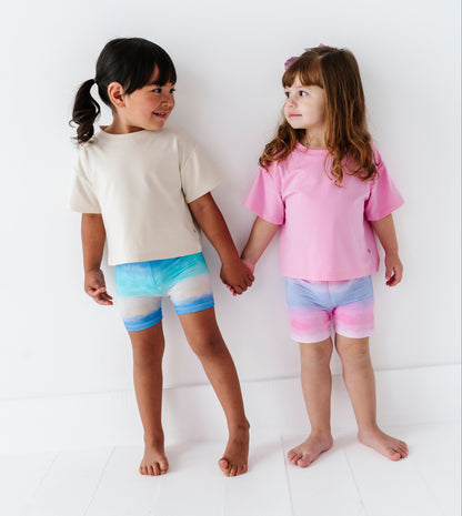 Two children holding hands, wearing colorful bamboo biker shorts and t-shirts against a white background