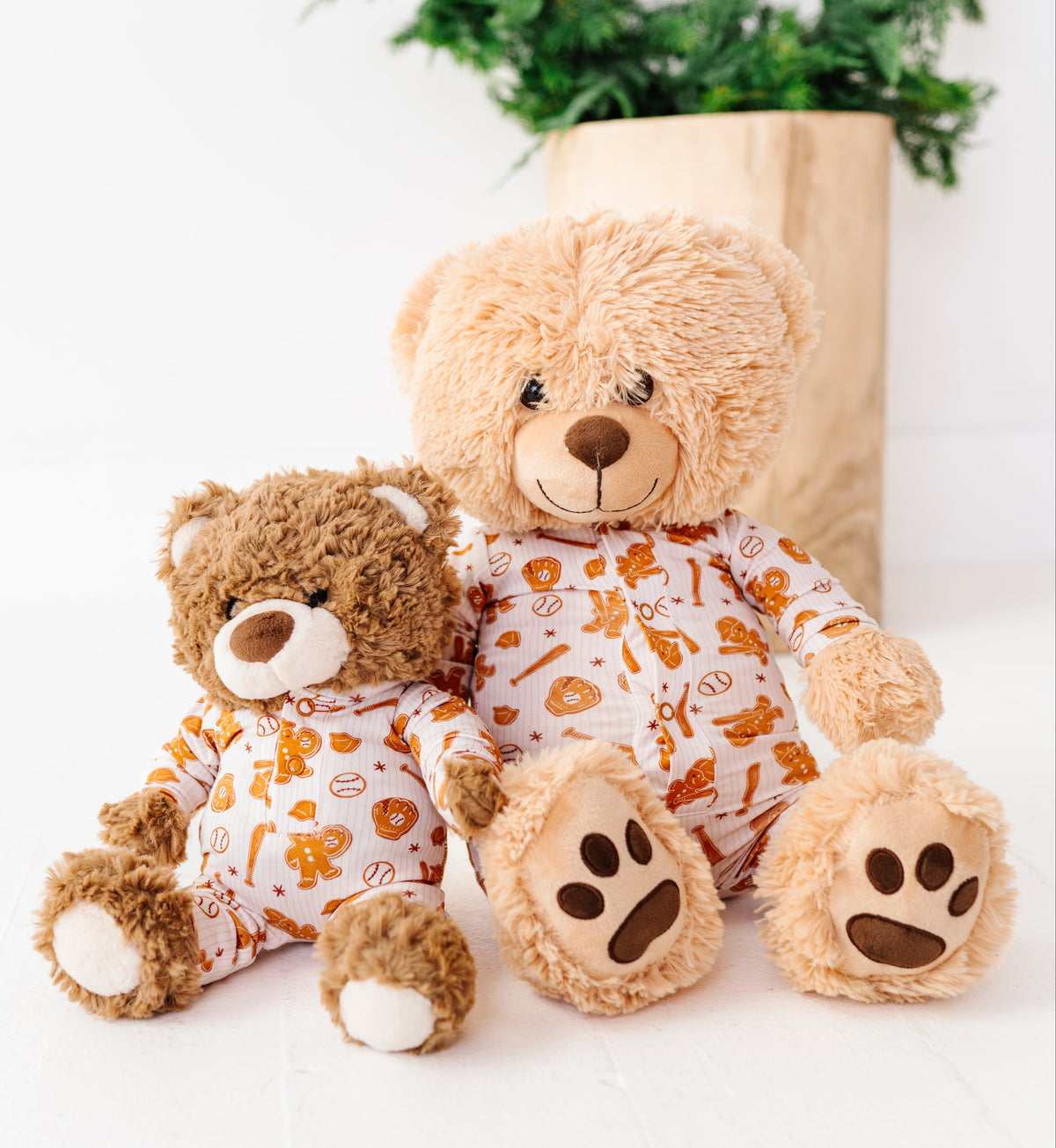 Two plush teddy bears in matching white pajamas with orange and yellow food-themed prints, posed in front of a kraft paper bag and a green wreath on a white background.