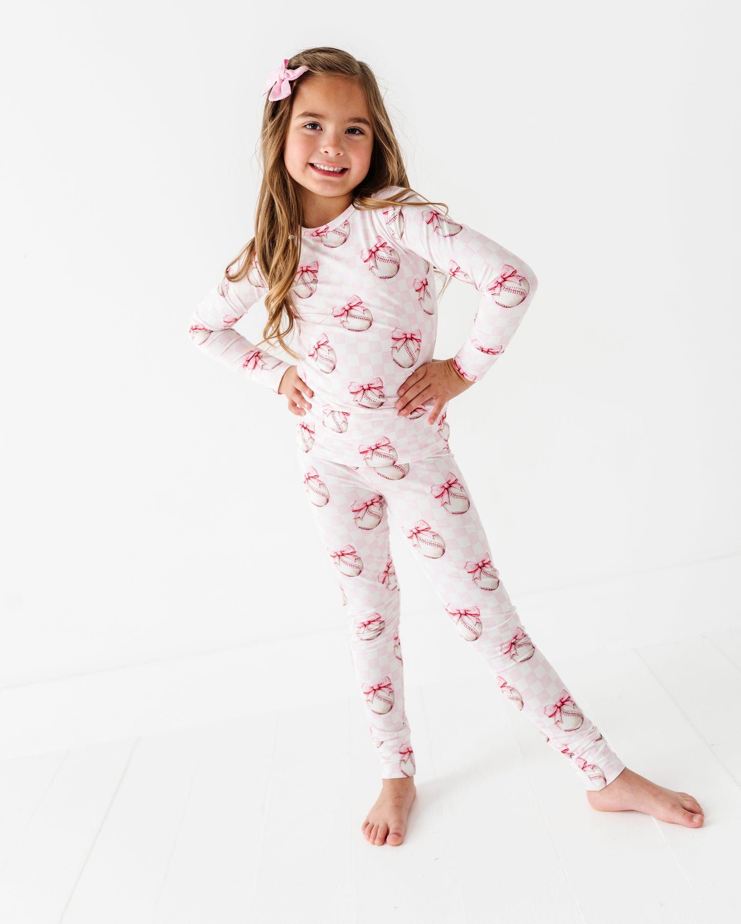 Young girl wearing a white pajama set with pink and white baseball pattern on a white background