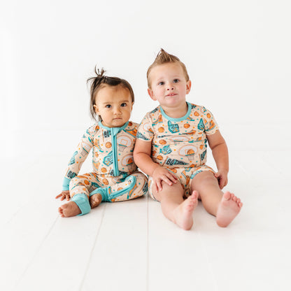Two children wearing sports-themed bamboo pajamas sitting on a white surface.