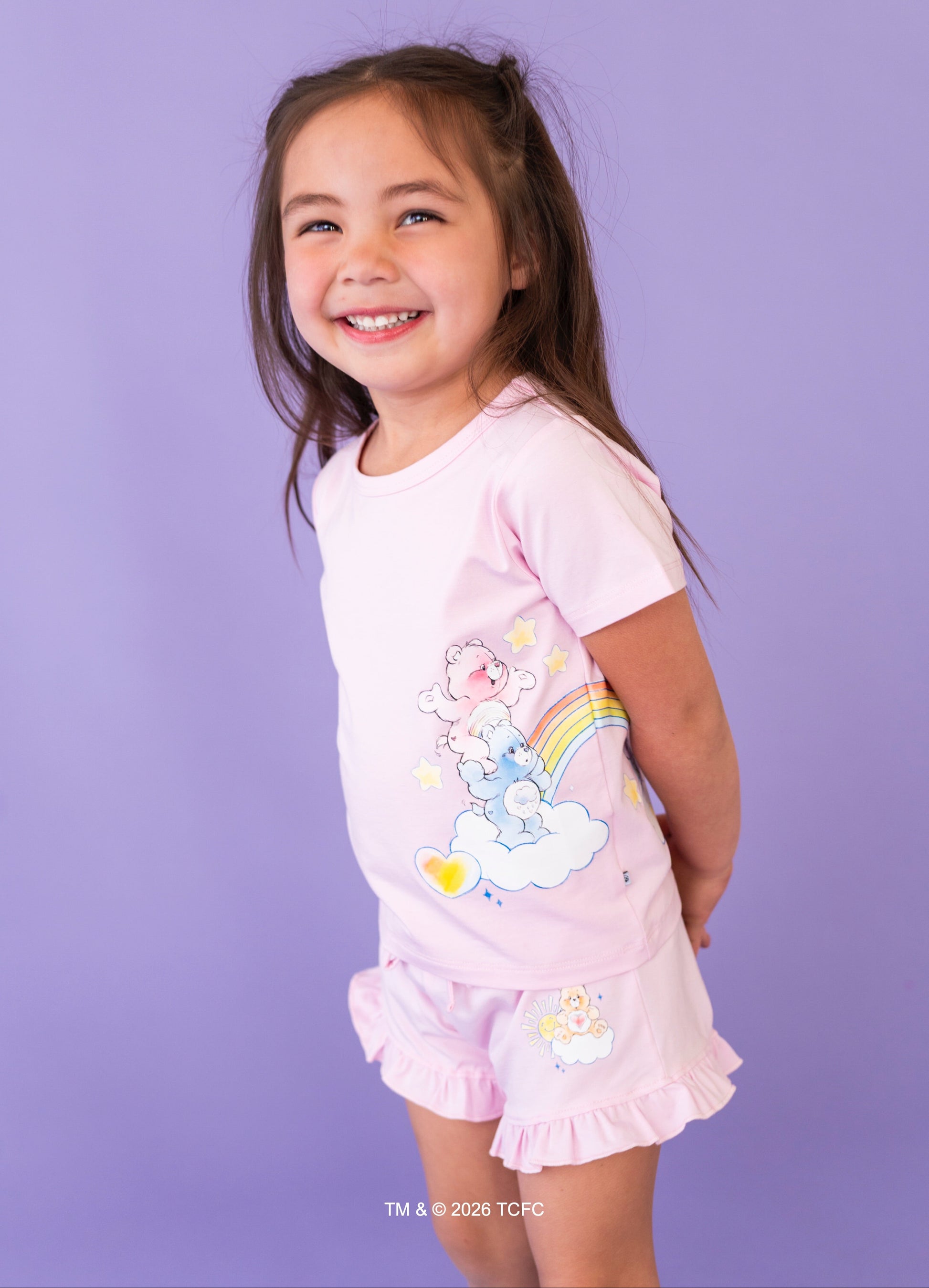 Young girl wearing a lilac outfit with Care Bears™ design against a purple background