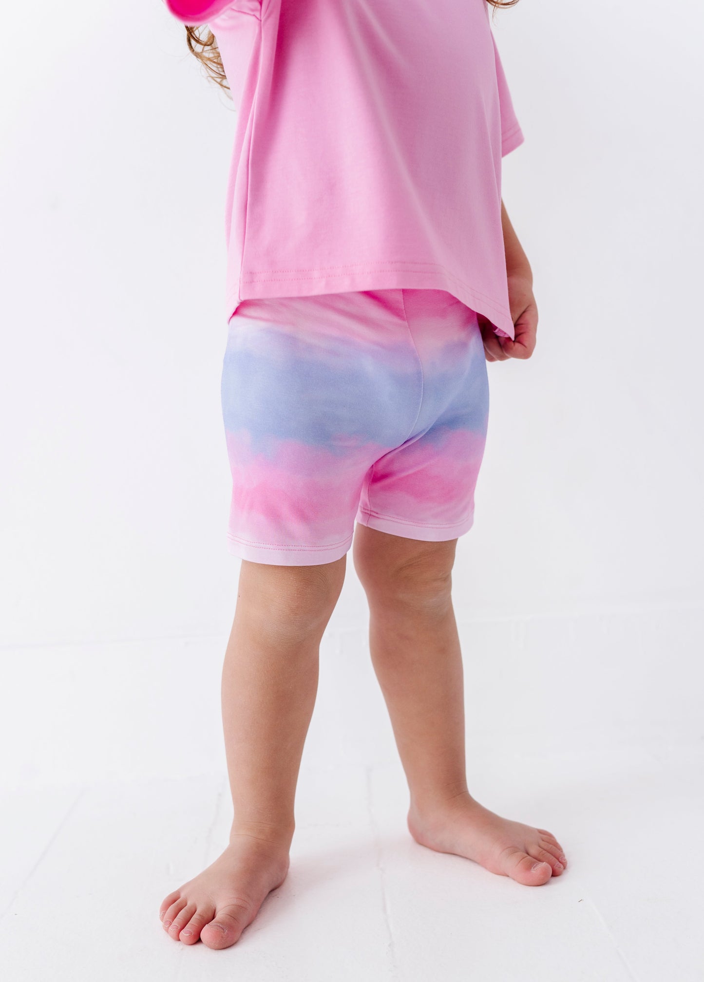 Young girl wearing a pink top and colorful bamboo biker shorts on a white background