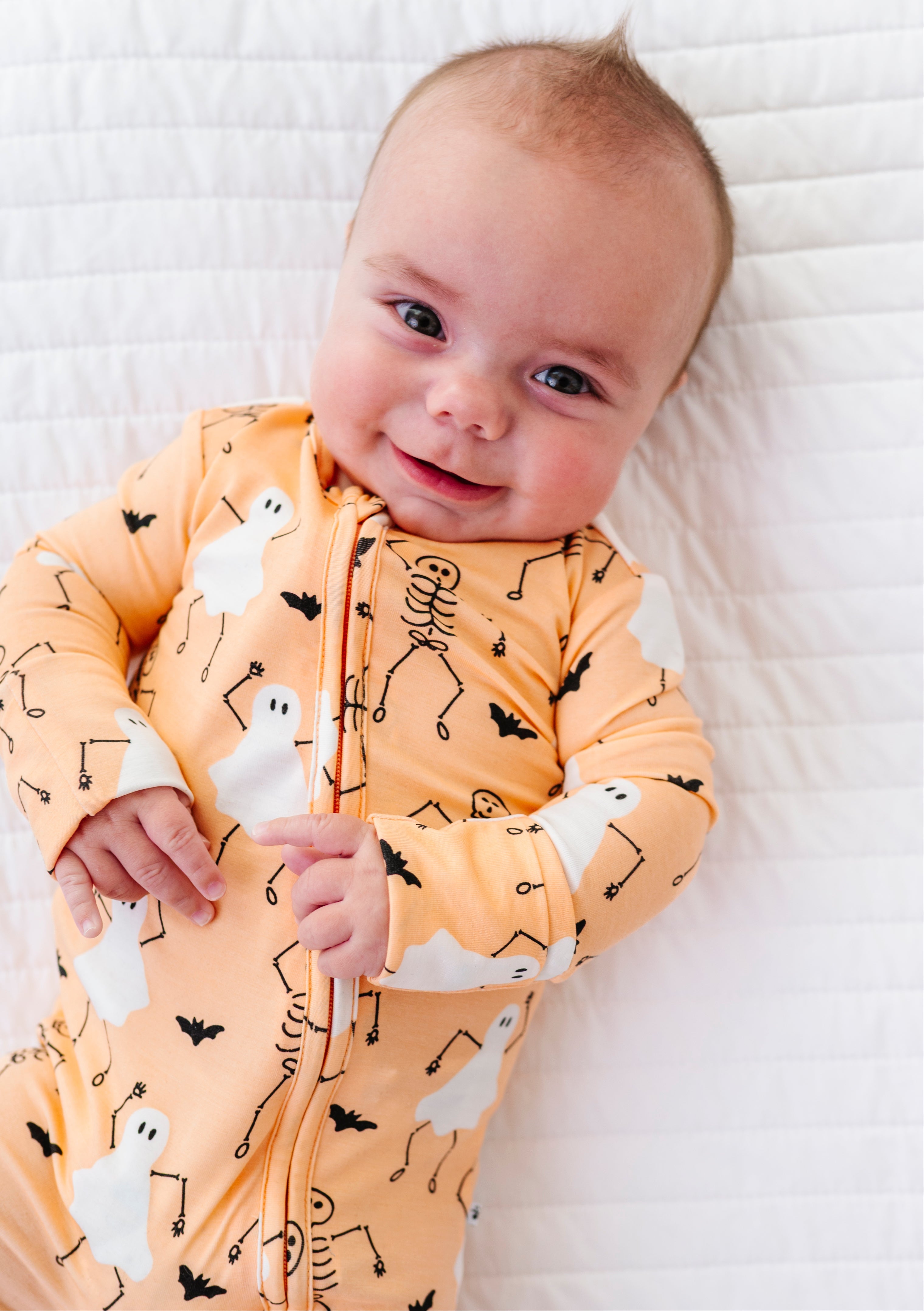 Baby wearing a Halloween-themed onesie on a white blanket