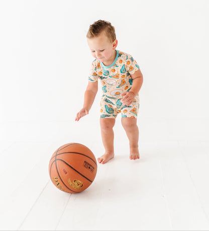 Child in a sports-themed bamboo onesie standing next to a basketball on a white background