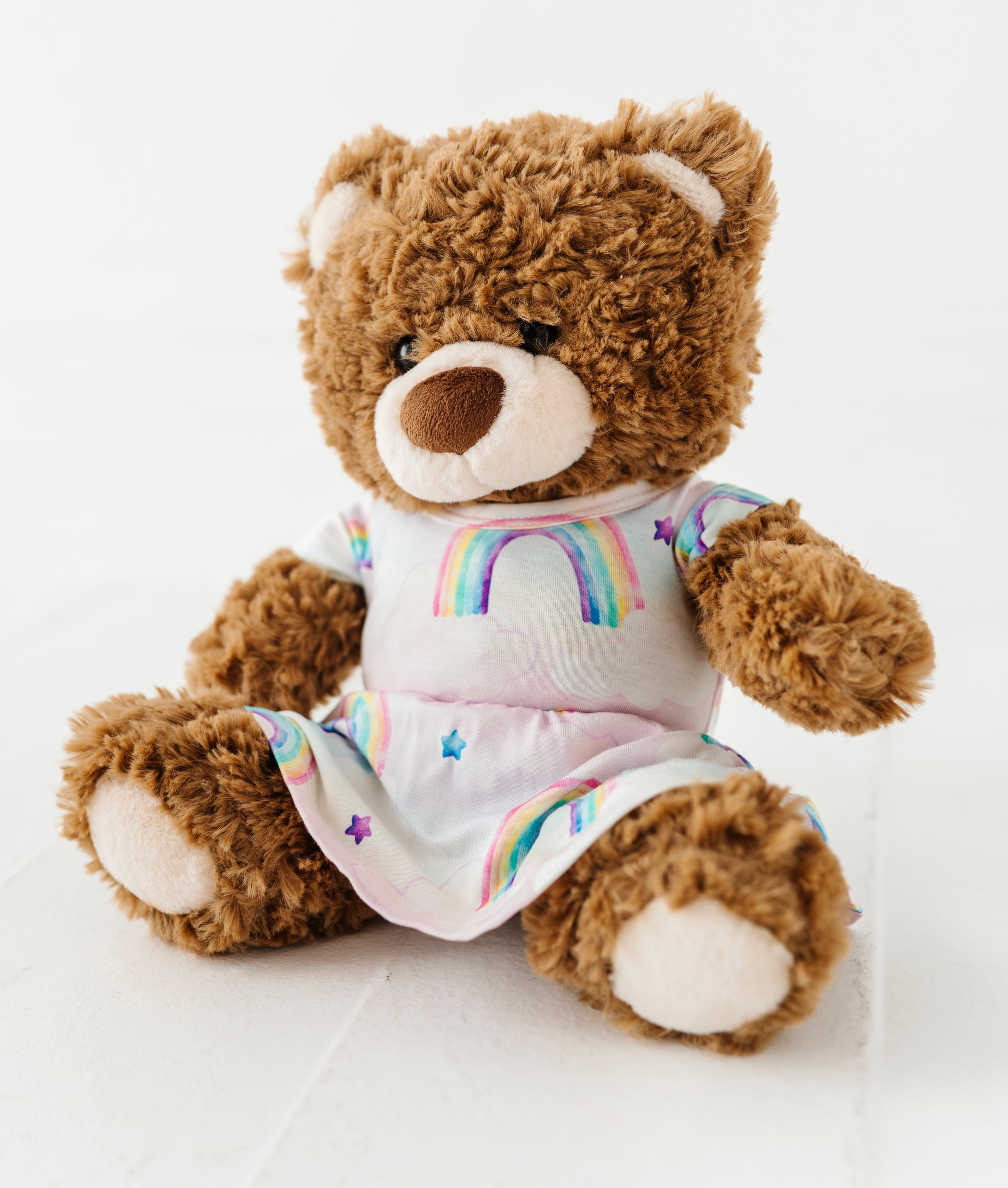 Brown teddy bear wearing a bamboo dress with a watercolor rainbow design on a white background