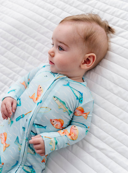 Baby wearing a romper with fish pattern lying on a textured white surface