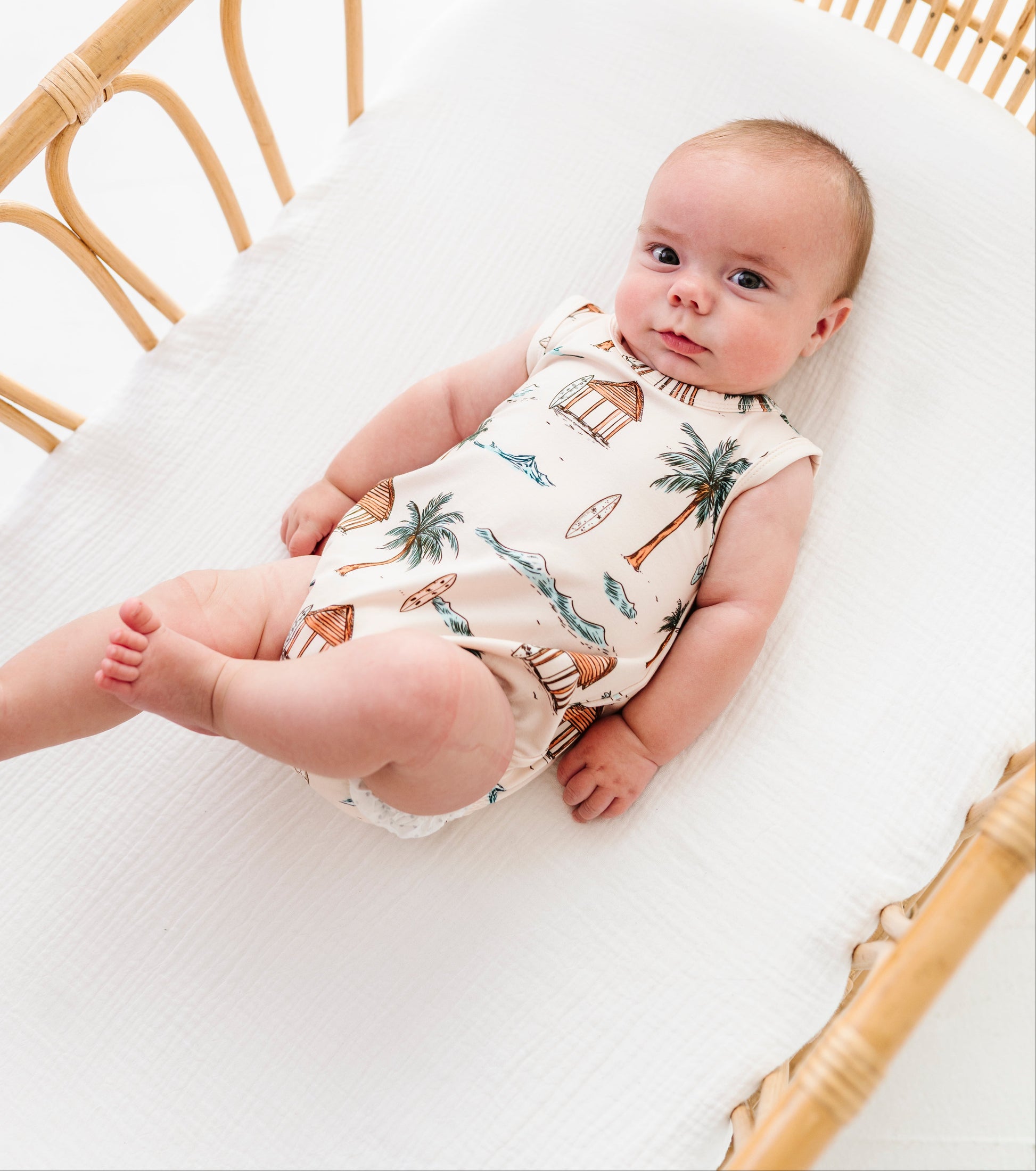 Baby lying in a crib wearing a patterned onesie with a white background