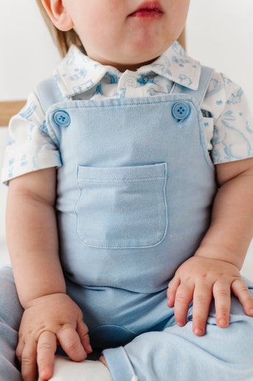 Child wearing a light blue outfit with a white shirt and blue overalls.