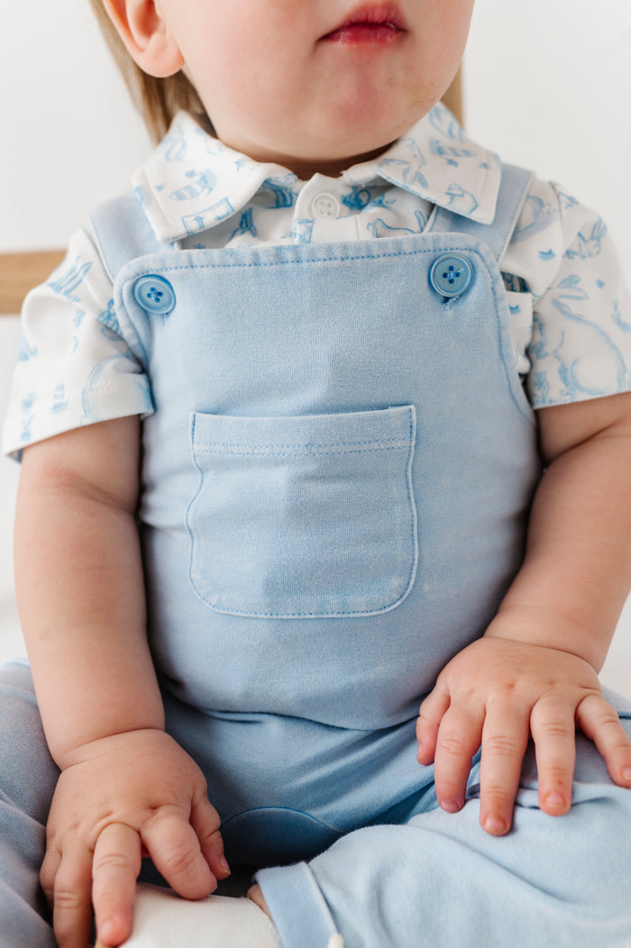 Child wearing a light blue outfit with a white shirt and blue overalls.