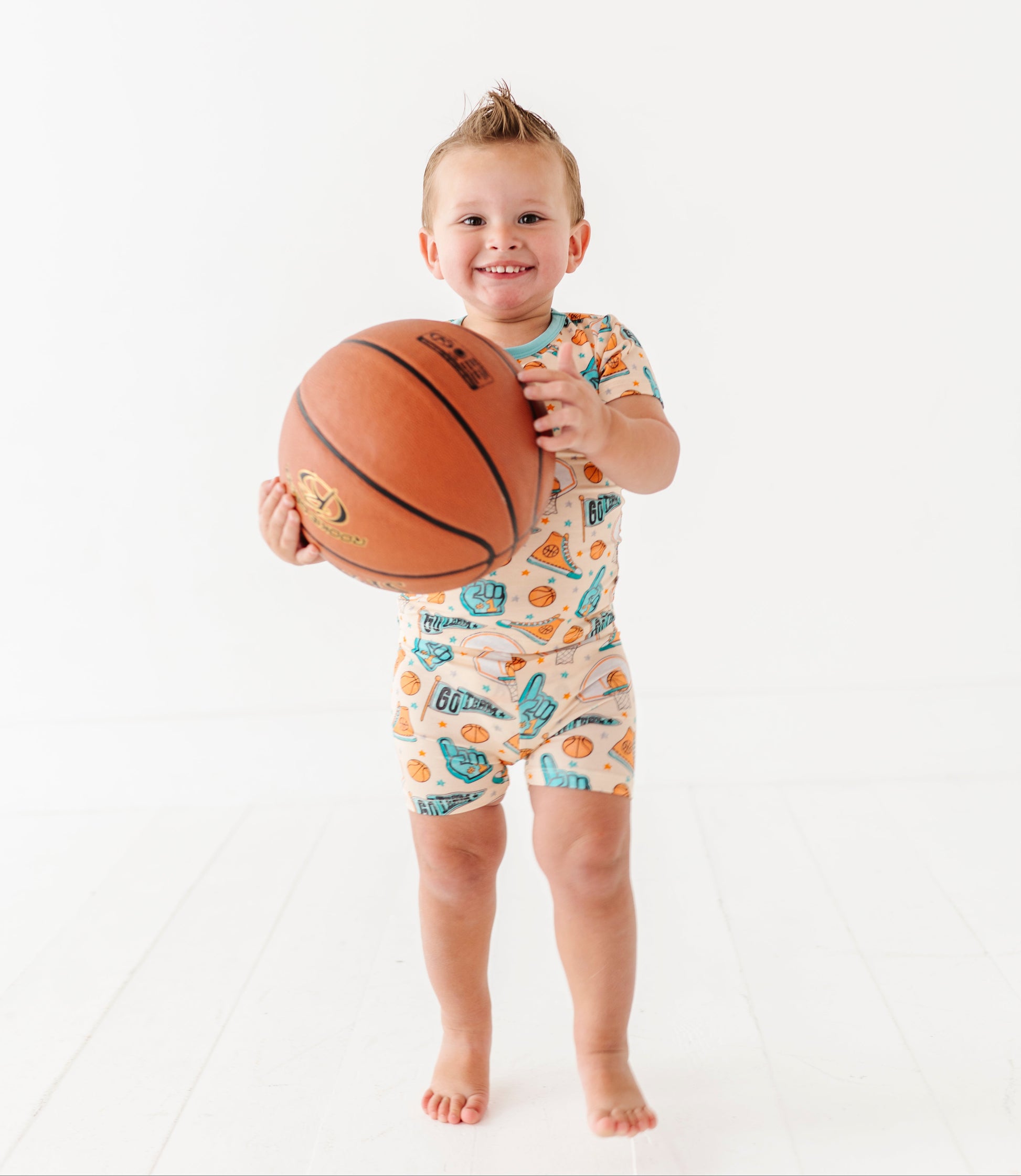Child holding a basketball wearing a sports themed onesie on a white background