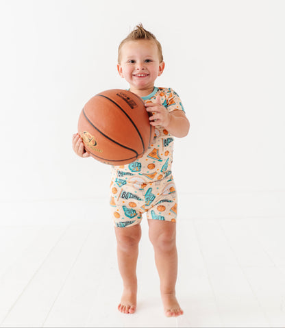 Child holding a basketball wearing a sports themed onesie on a white background