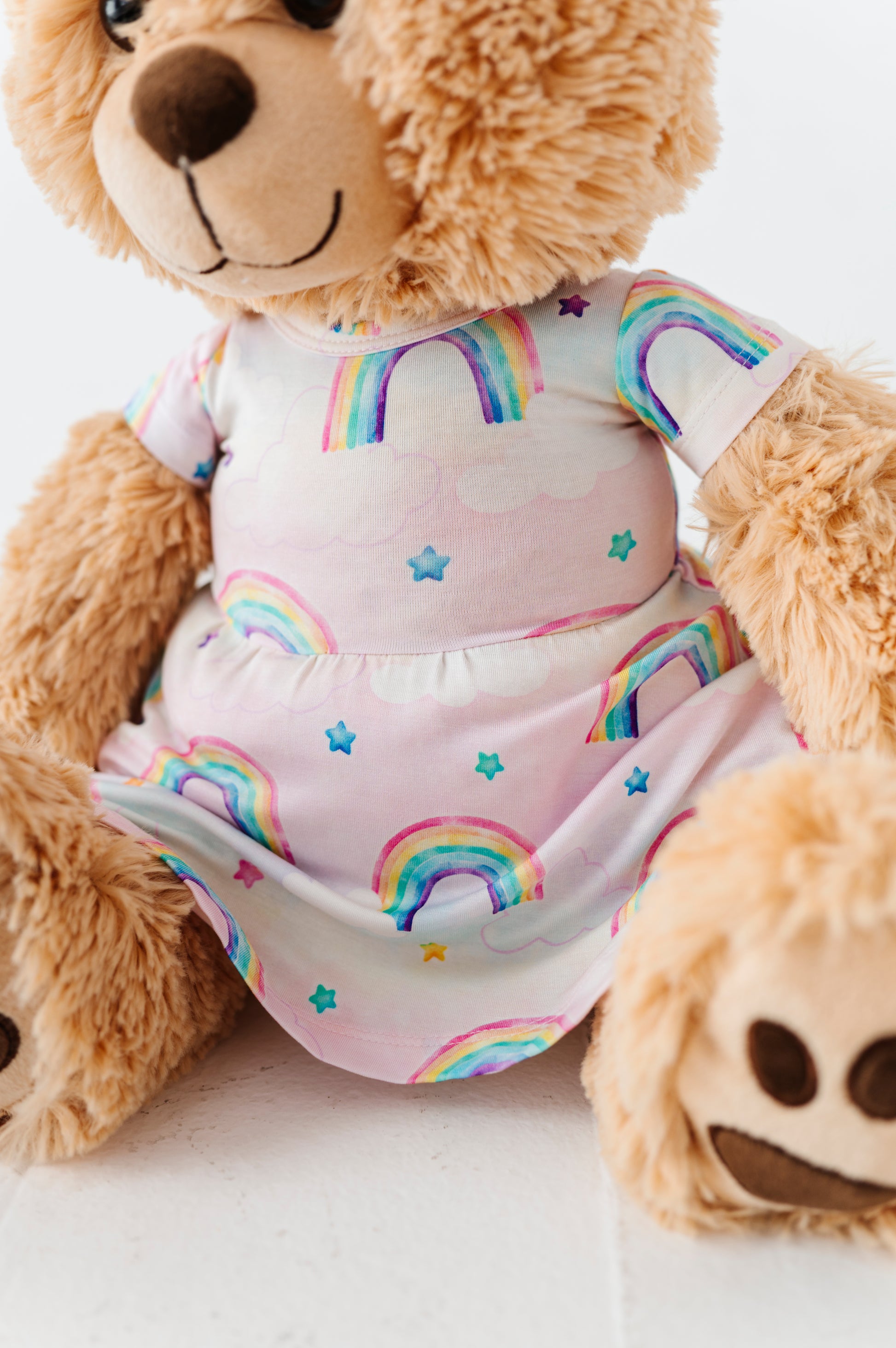 Teddy bear wearing a bamboo dress with watercolor rainbow patterns on a white background