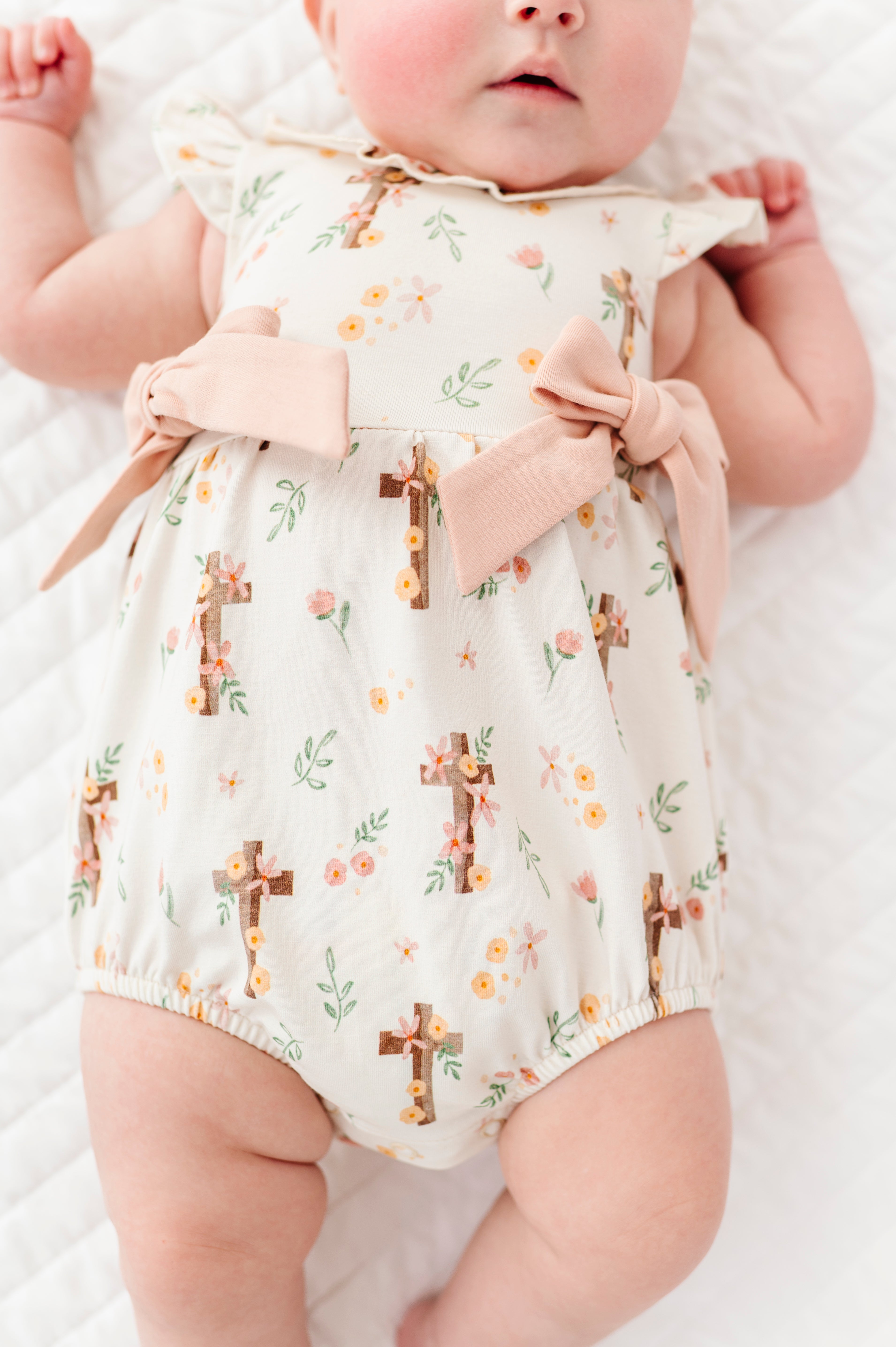 Baby wearing a floral Easter bamboo romper with cross patterns on a white background