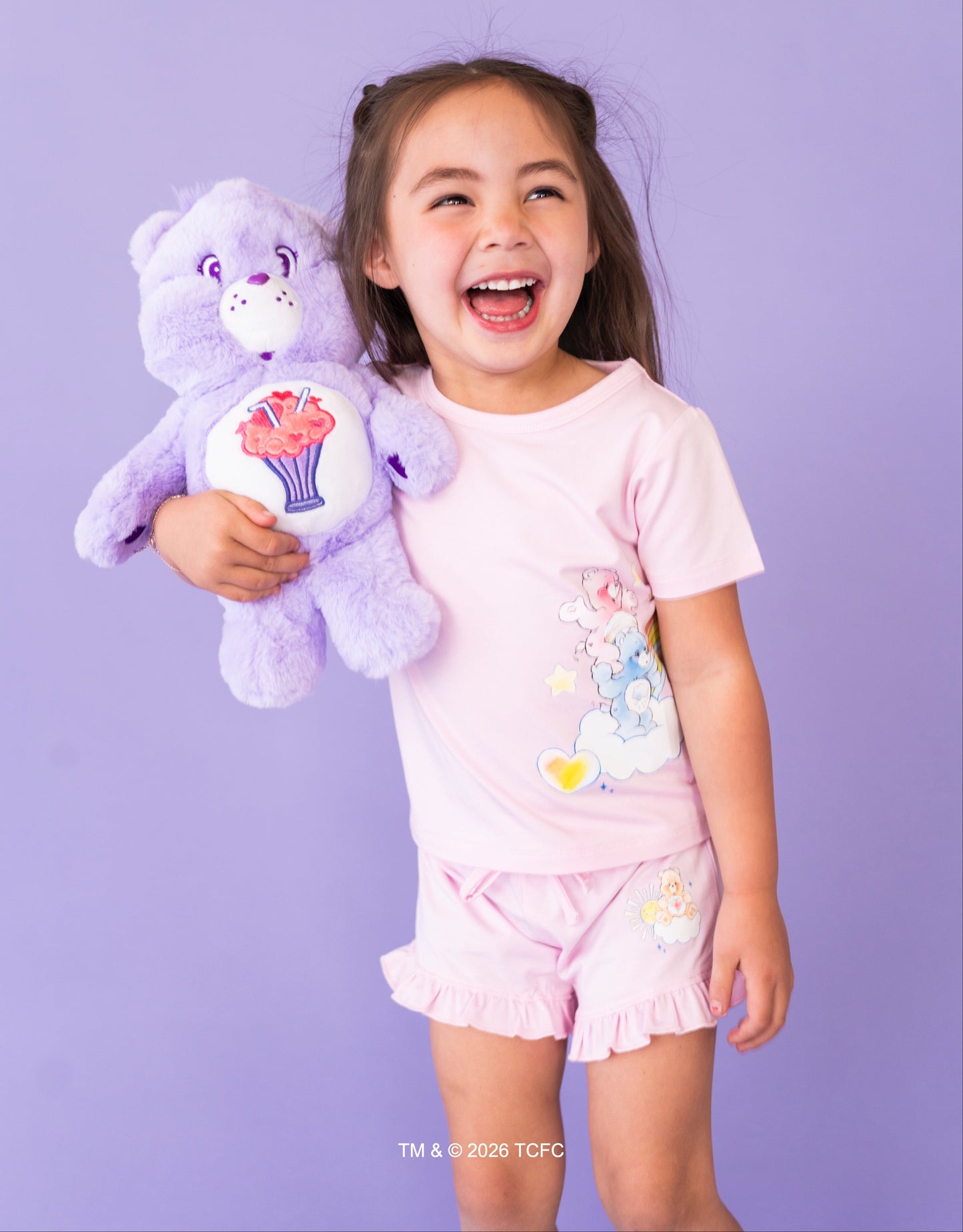 Child holding a purple Care Bears™ plush against a purple background