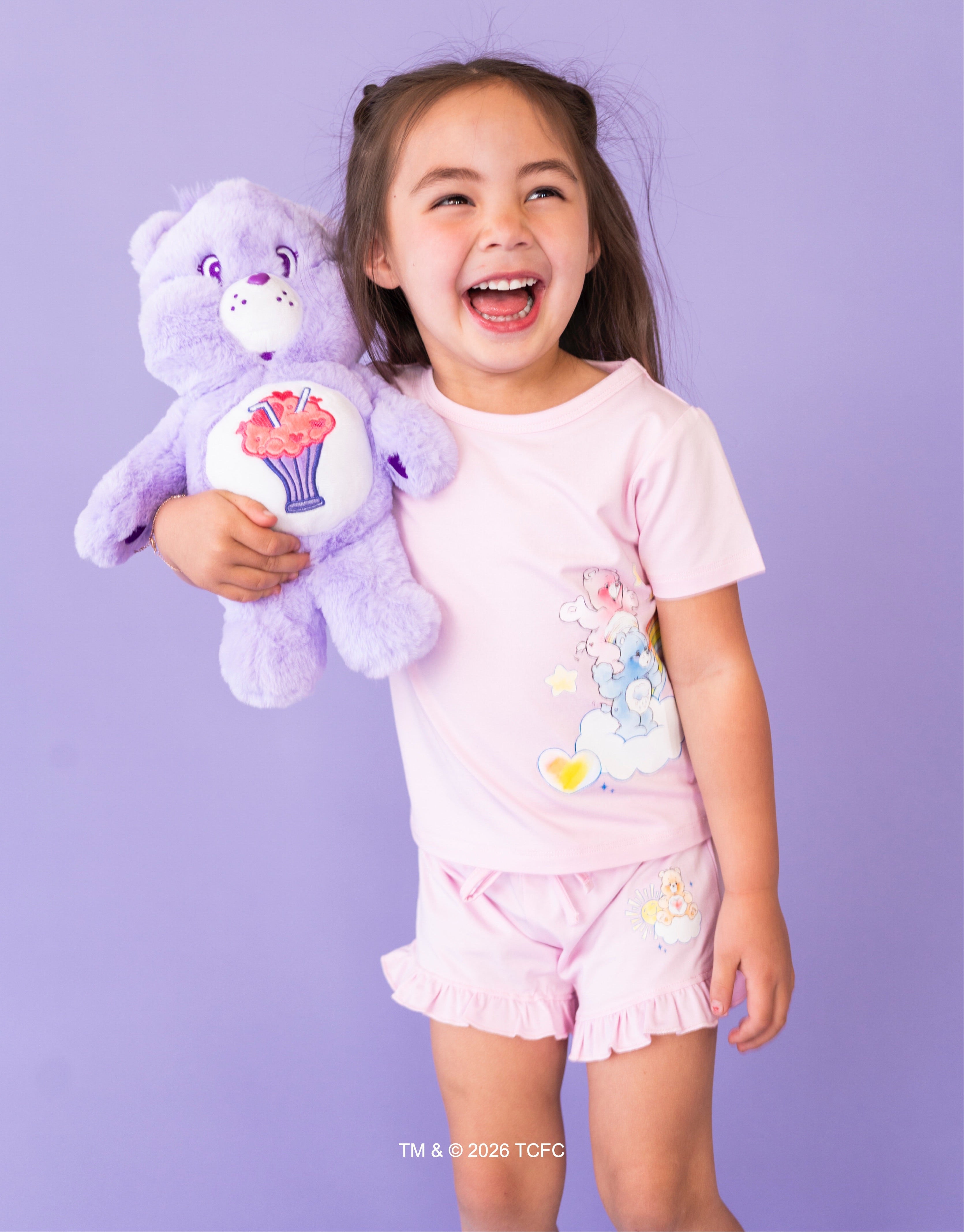 Child holding a purple care bear with a smiling face against a purple background