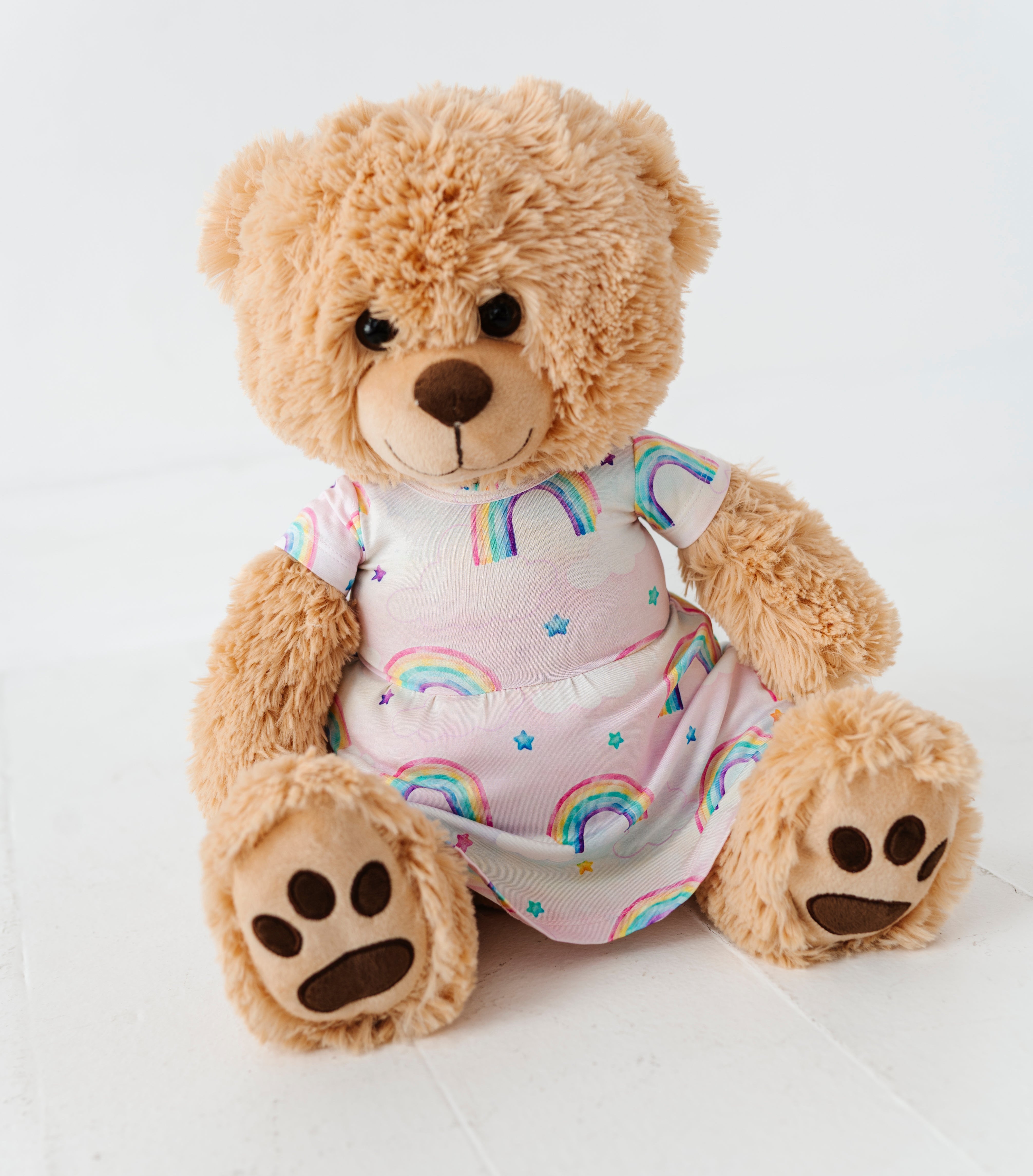 Teddy bear wearing an outfit with rainbow pattern on a white background