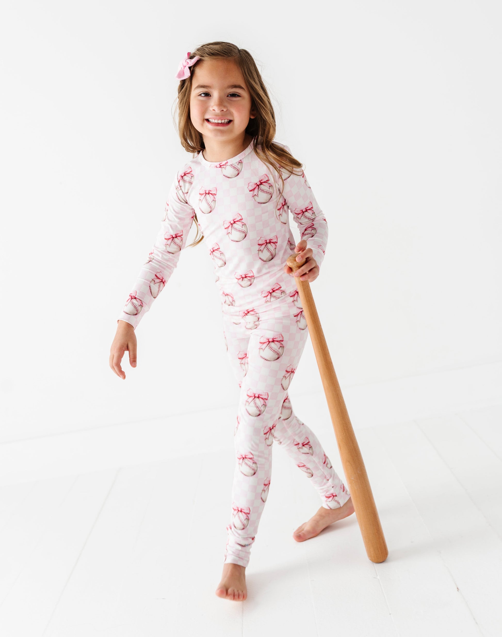 Young girl in a white bamboo pajama set  holding a wooden bat, on a white background