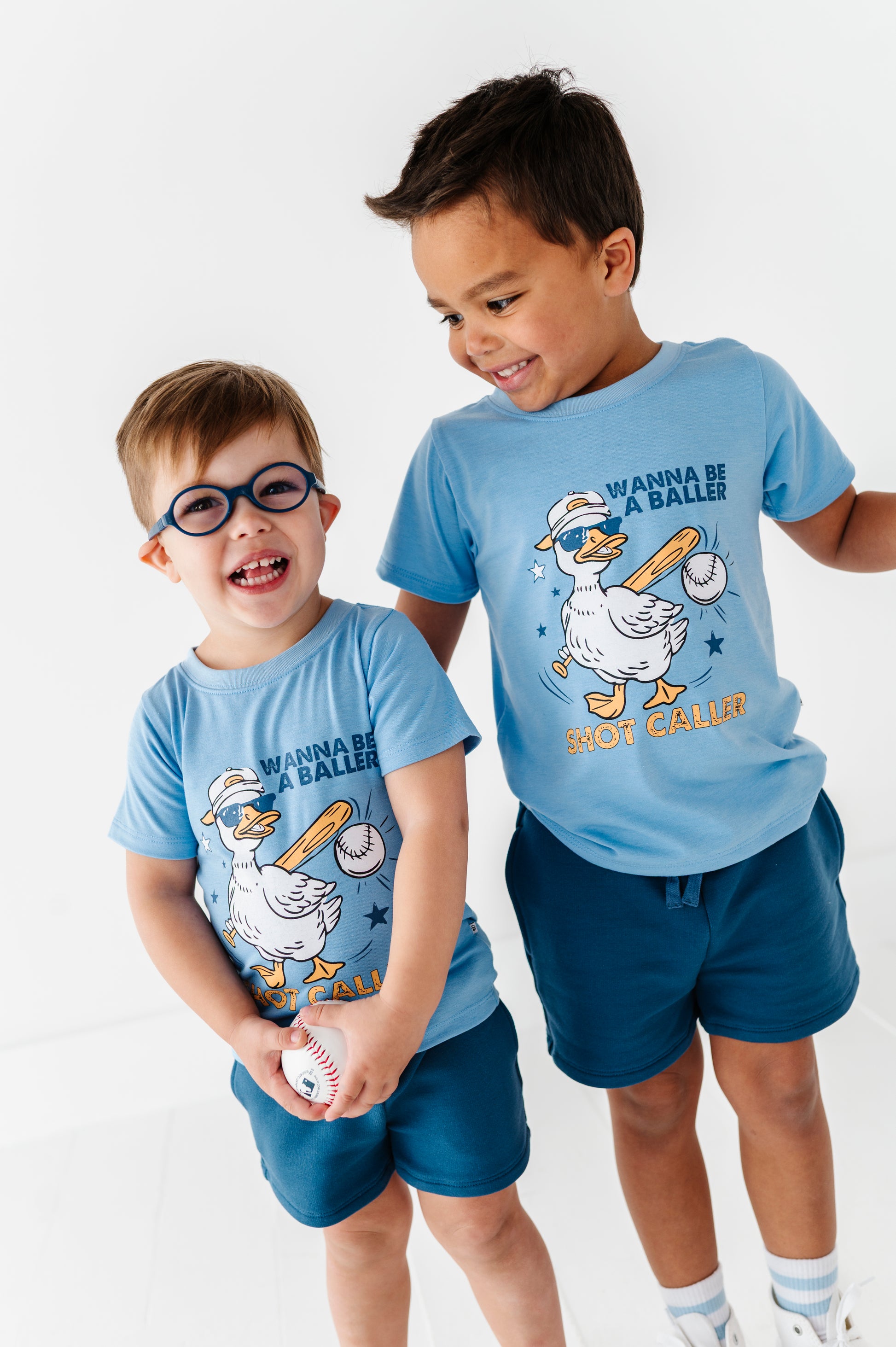 Two children wearing matching baseball-themed t-shirts against a white background 