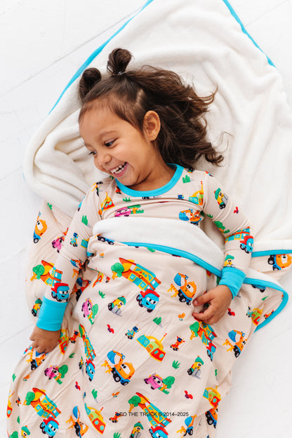 Toddler girl wearing Leo the Truck two-piece bamboo pajamas, wrapped in a coordinating bamboo blanket 
