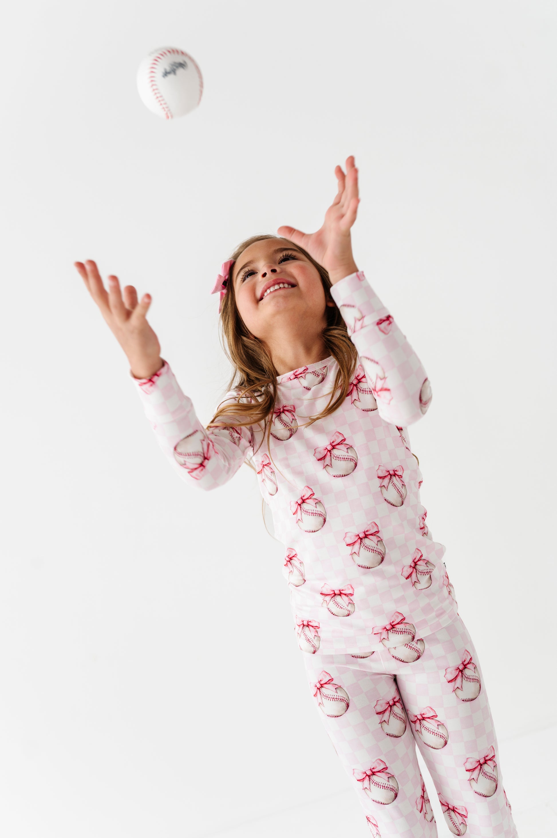Girl in bamboo pajamas with bow pattern tossing a ball on a white background
