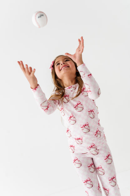 Girl in bamboo pajamas with bow pattern tossing a ball on a white background