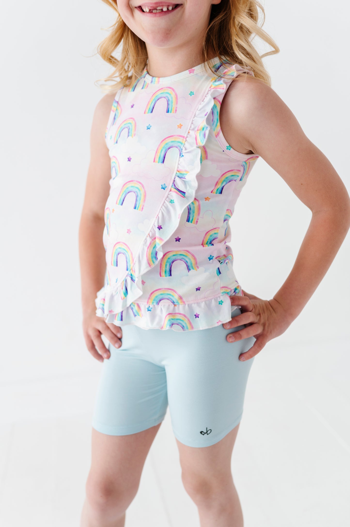Child wearing a sleeveless bamboo cotton peplum top with watercolor rainbow pattern and light blue bamboo shorts on a white background