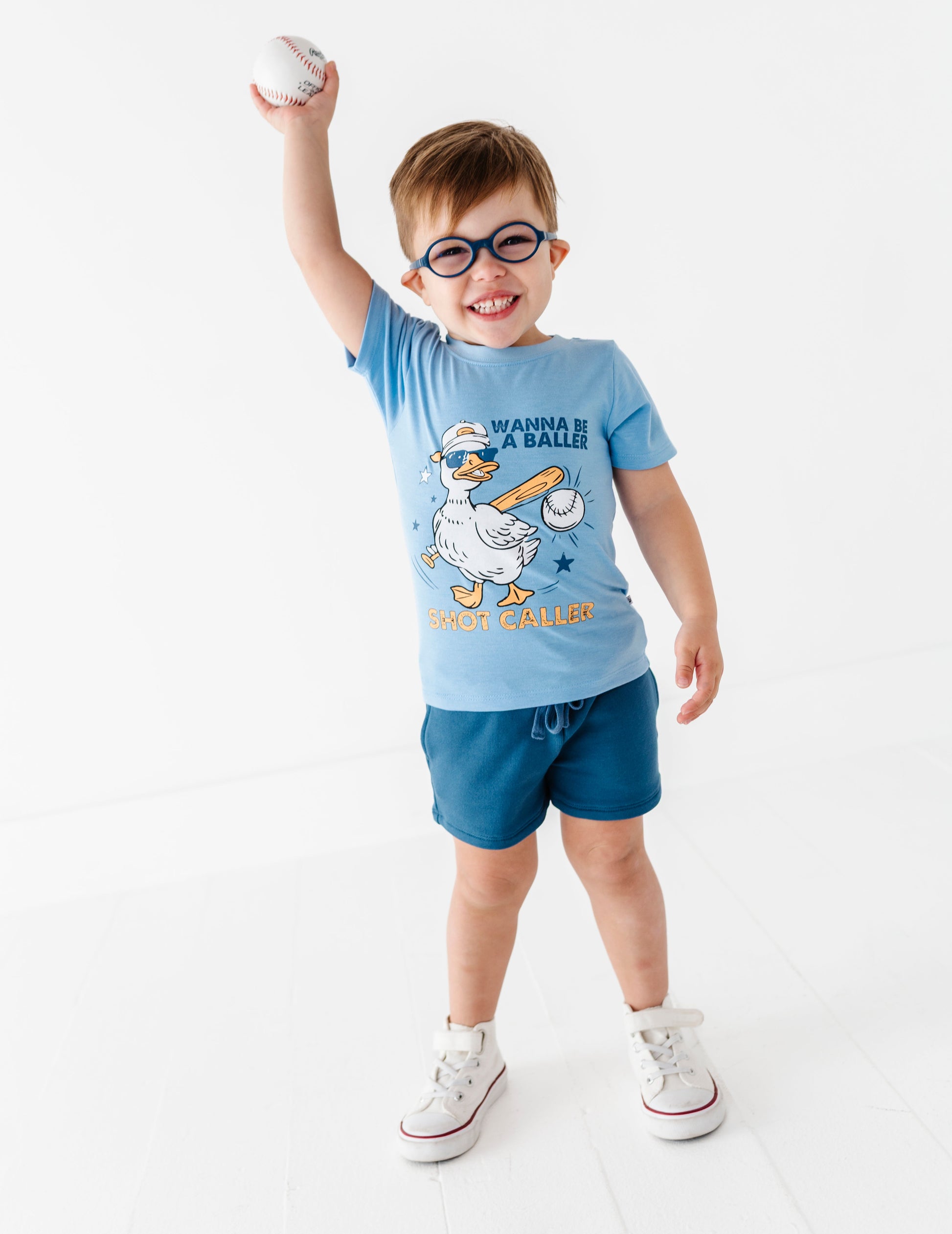 Child wearing a blue baseball t-shirt with a cartoon character and text, standing on a white background