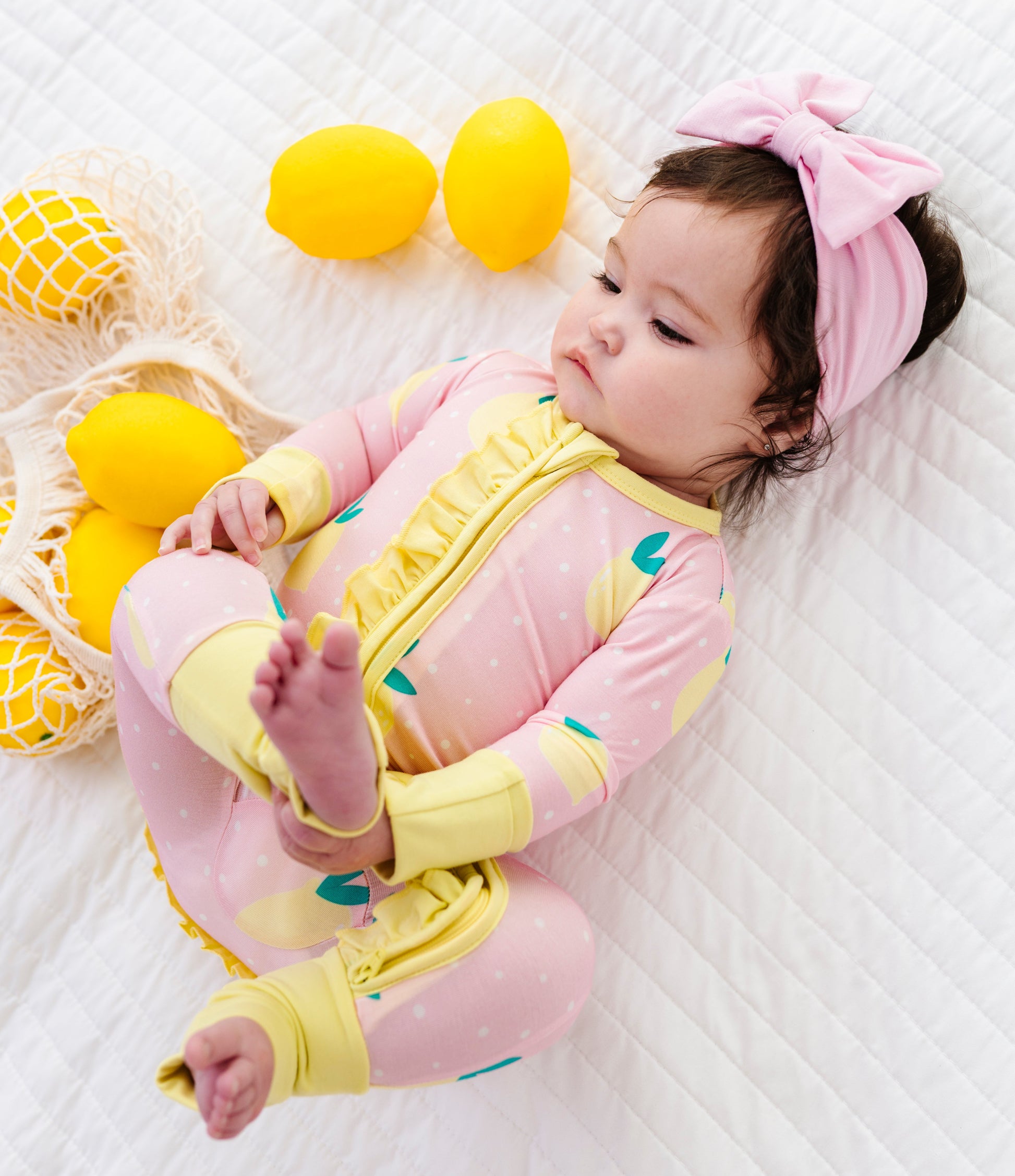 Baby in pink and yellow romper with lemons  on a white background