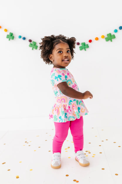 Child wearing a St. Patrick's Day bamboo cotton outfit with pink leggings, standing on a white background with confetti.