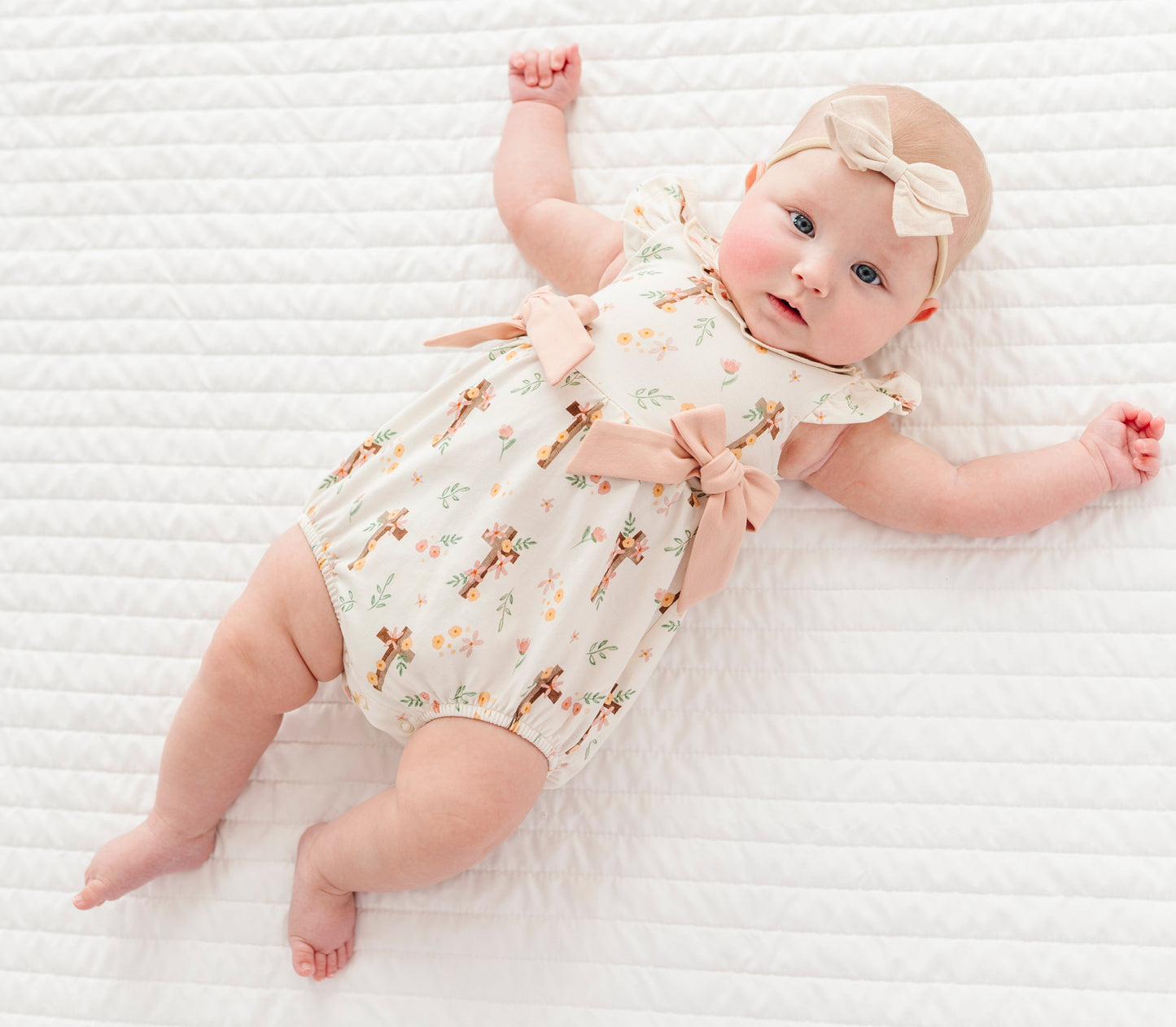baby girl in a cross with florals bubble romper and a neutral colored headband on a white background 