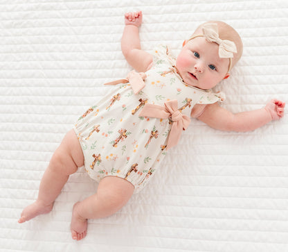 baby girl in a cross with florals bubble romper and a neutral colored headband on a white background 