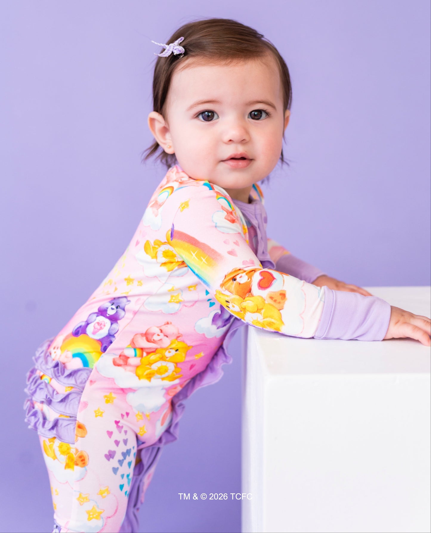 Child wearing a colorful rainbow-themed shirt against a purple background