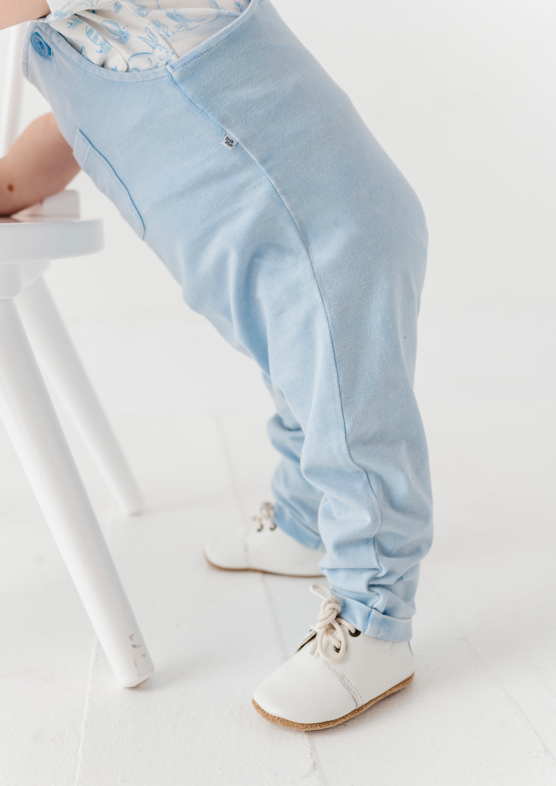 Light blue pants worn by a child standing by a white stool.