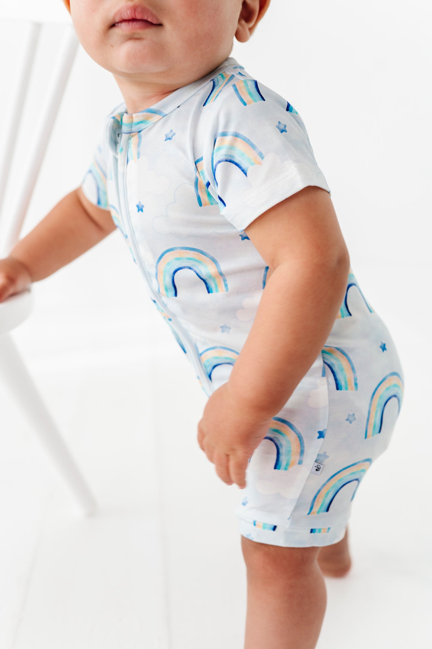 Child wearing a white bamboo romper with watercolor rainbow patterns on a white background