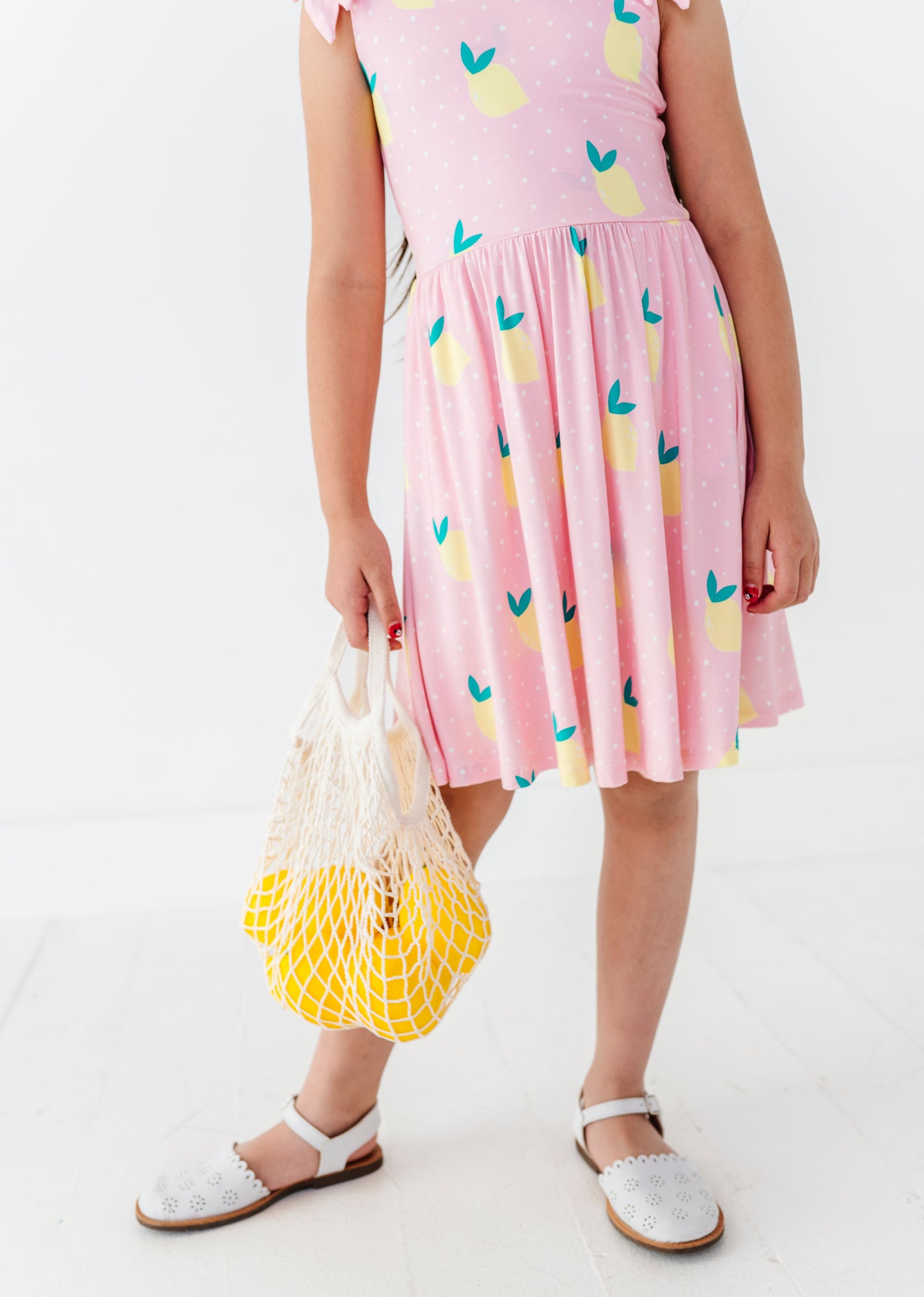 Girl wearing a pink dress with colorful patterns, holding a white bag with yellow mesh.